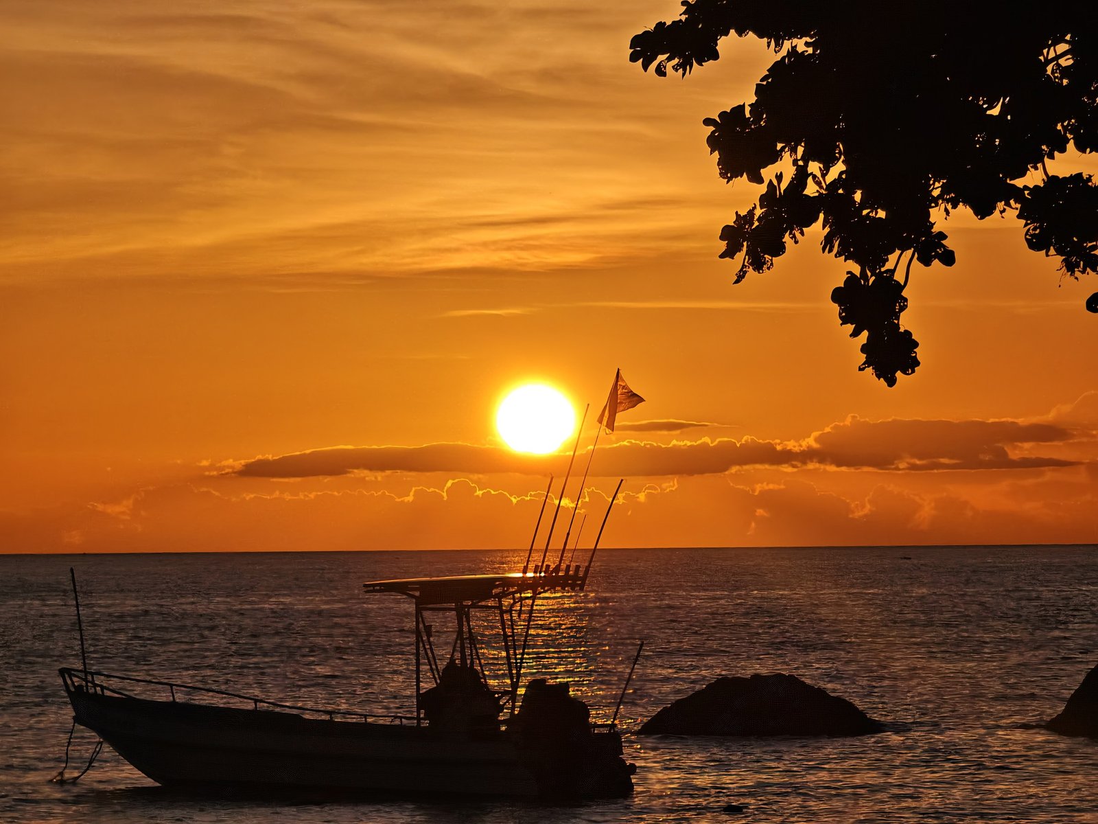 An intense orange sunset over the sea with a fishing boat in silhouette